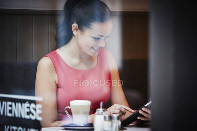 Jovem mulher sentada no café com comprimido digital e bebida quente — Fotografia de Stock
