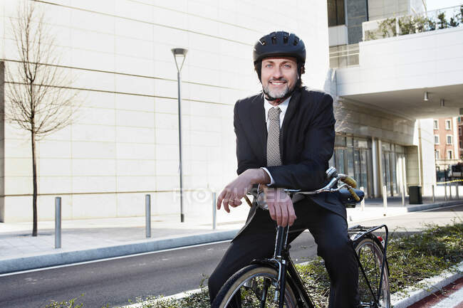 Mid adult businessman sitting on bike, smiling — Stock Photo