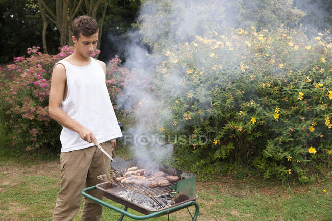 Junger Mann grillt Fleisch im Garten — Stockfoto