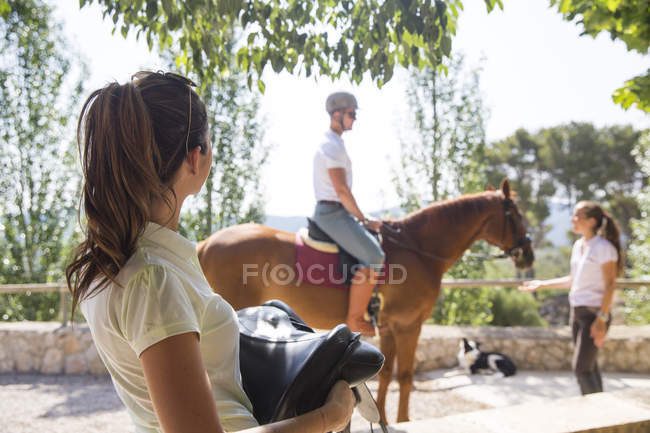 Female groom carrying saddle at rural stables — Stock Photo