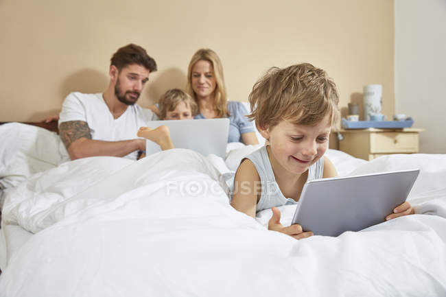 Mãe e pai na cama com filhos usando a tecnologia — Fotografia de Stock