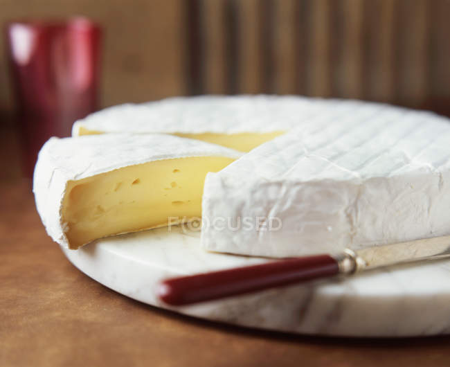 Brie rodada com faca de queijo na placa de corte de mármore — Fotografia de Stock
