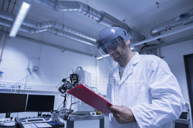 Lab assistant checking detail of research on clipboard — Stock Photo