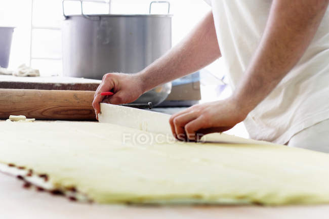 Abgeschnittenes Bild vom Bäcker, der Teig schneidet — Stockfoto