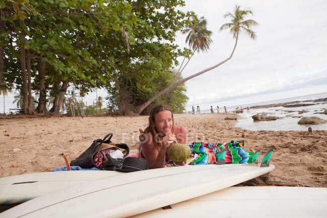 Чоловік лежить на пляжі п'є кокосове молоко — стокове фото