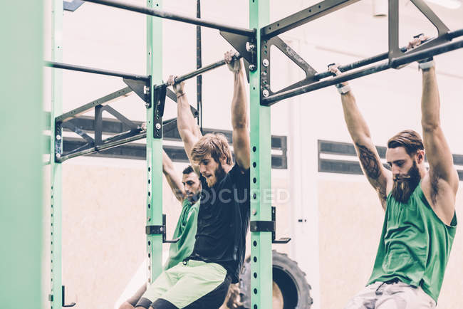 Trois entraîneurs masculins s'entraînent sur le bar d'exercice dans la salle de gym — Photo de stock