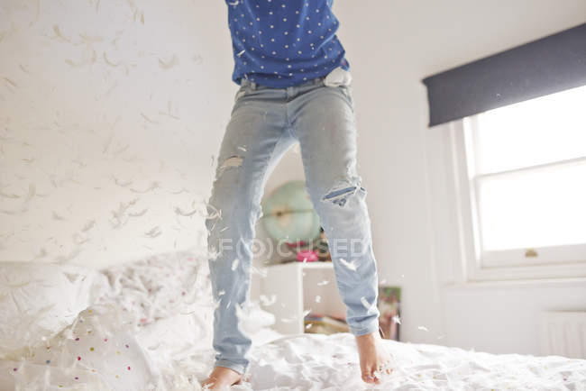 Талія вниз дівчина стрибає і пір'я подушка бореться на ліжку — стокове фото