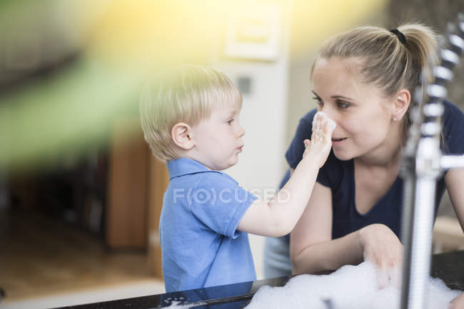 Mother and son doing washing up together, playing with bubbles — Stock Photo