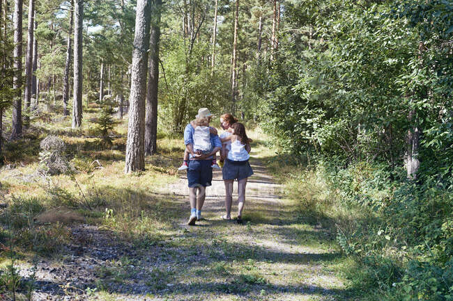 Parents giving daughters piggy back through forest — Stock Photo