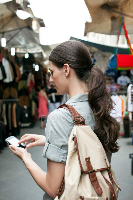 Mensajes de texto de mujer joven en el teléfono celular, Mercado de San Lorenzo, Florencia, Toscana, Italia - foto de stock