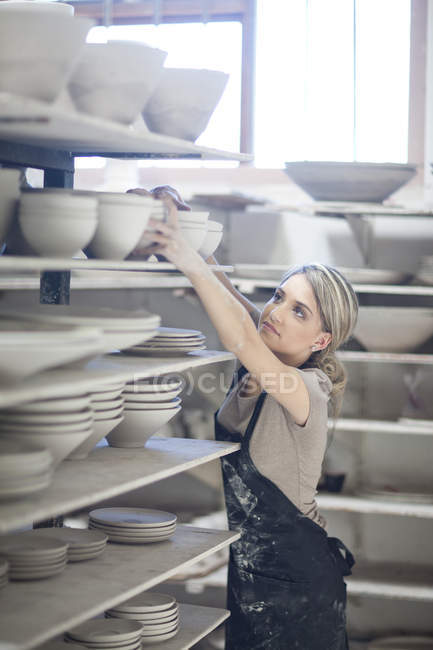 Potter apilar cuencos en el estante en la fábrica de vajilla - foto de stock