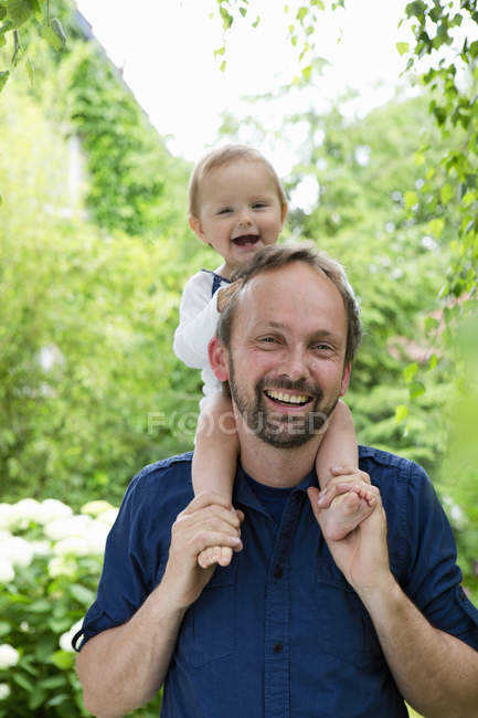 Portrait of baby girl sitting on father shoulders in garden — Stock Photo