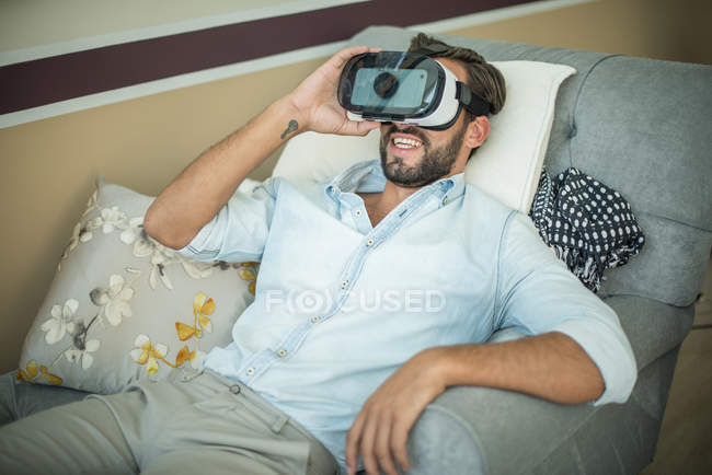 Jovem em poltrona olhando através de fone de ouvido realidade virtual — Fotografia de Stock