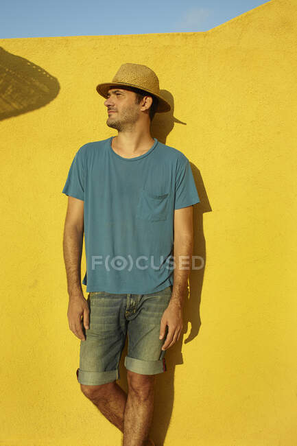 Homem adulto intermediário pela parede amarela, olhando afastado — Fotografia de Stock