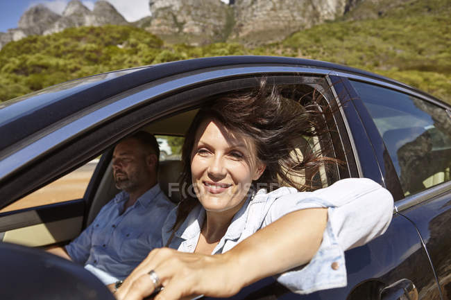 Couple in car, driving along rural road, woman leaning on open window — Stock Photo