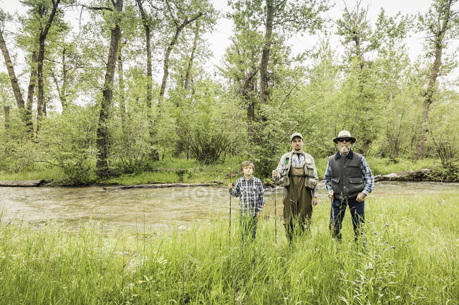 Front view of multi generation family standing on riverbank holding fishing rods — Stock Photo