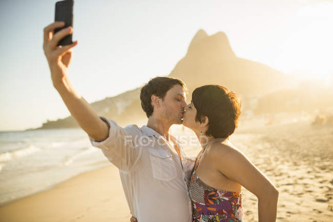 Parejas jóvenes fotografiándose besándose, Ipanema Beach, Rio, Brazil - foto de stock