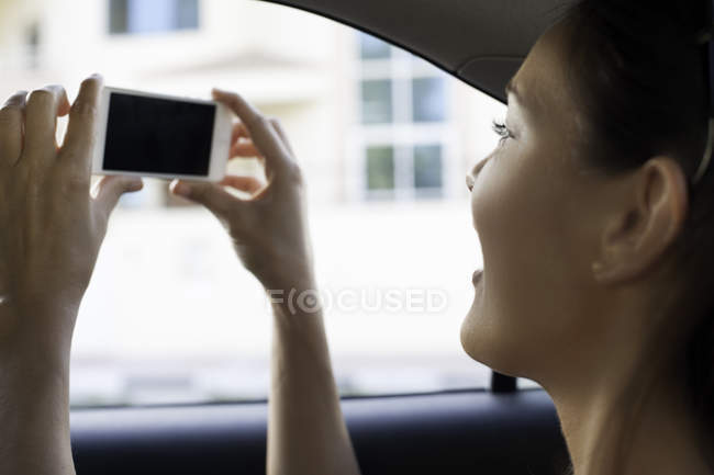 Close up of young woman photographing from taxi window — Stock Photo