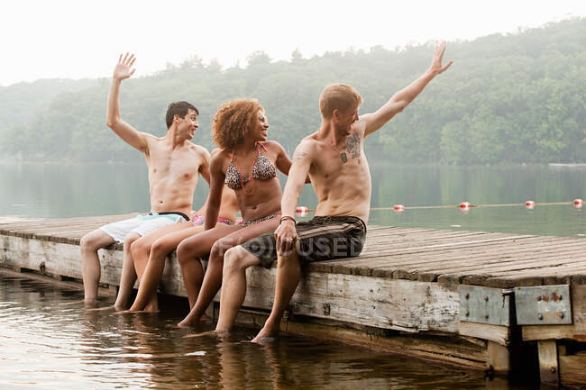 Friends turning to wave from pier on lake — Stock Photo