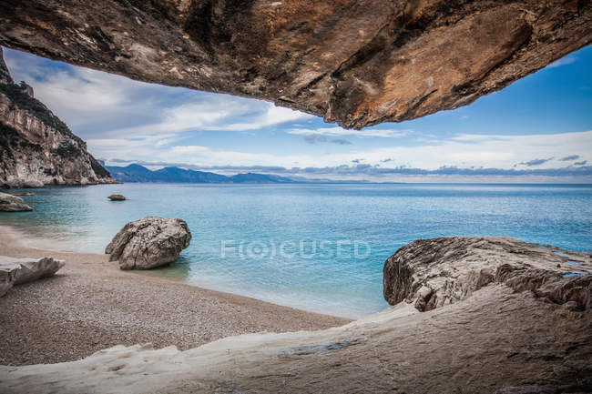 View of coastline and rocky beach under blue sky from cave — Stock Photo