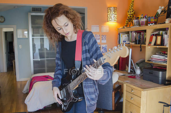 Adolescente tocando la guitarra eléctrica en el dormitorio - foto de stock
