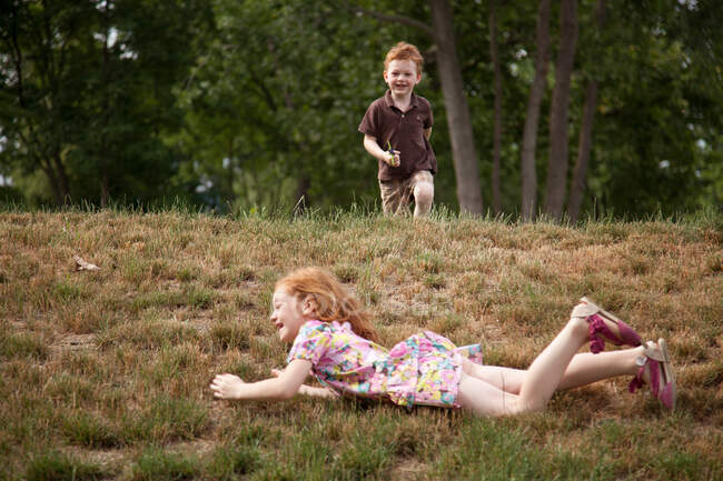 Menina rolando colina abaixo, menino correndo — Fotografia de Stock