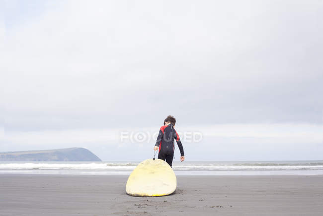 Rear view of boy pulling surfboard on beach — Stock Photo