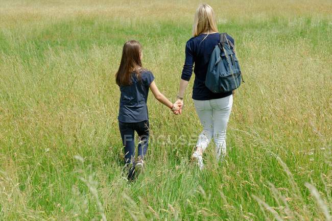 Вид ззаду мати і дочка прогулюються довгим трав'яним полем — стокове фото