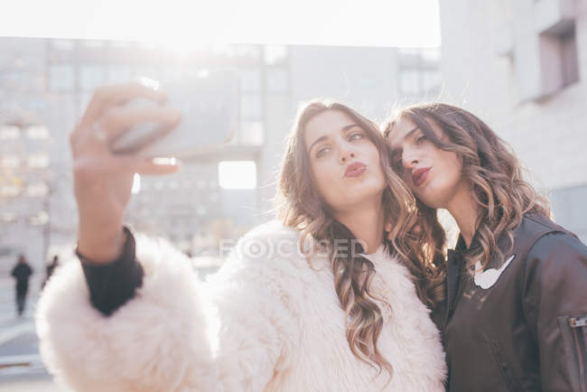 Twin sisters, outdoors, taking selfie, using smartphone — Stock Photo