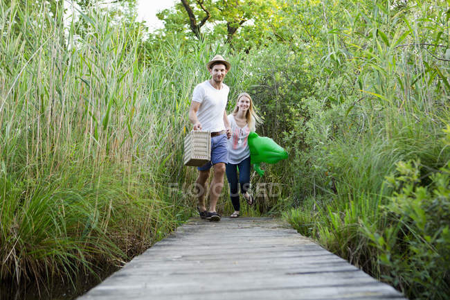 Mid adult couple running along pier at lakeside — Stock Photo
