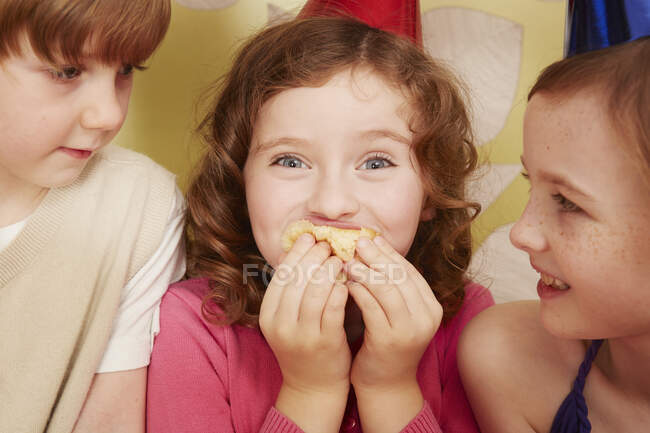 Menina comendo comida de festa, amigos assistindo — Fotografia de Stock