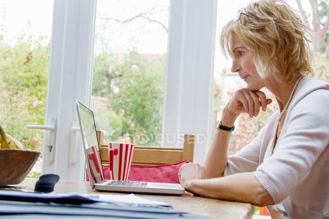 Mature woman using laptop in kitchen — Stock Photo