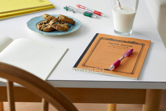 Kitchen table still life with notebooks, biscuits and milk — Stock Photo