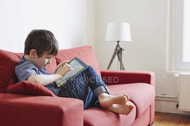 Boy using digital tablet on coach indoors — Stock Photo