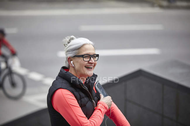 Mature woman training in city, listening to earphone music from smartphone — Stock Photo