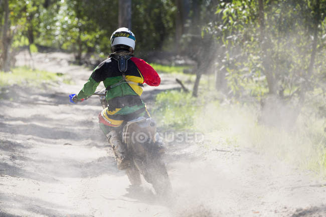 Rear view of young male motocross rider racing on forest track — Stock Photo