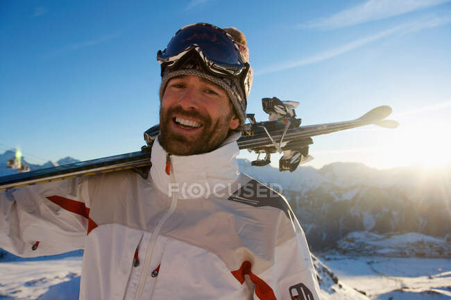 Retrato de um esquiador segurando esquis nas montanhas — Fotografia de Stock