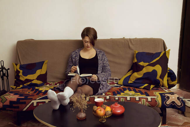 Молода жінка розслабляється на дивані читаючи свою книгу — стокове фото