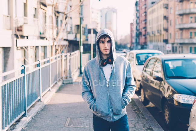 Man in urban area wearing hooded top and headphones looking at camera — Stock Photo