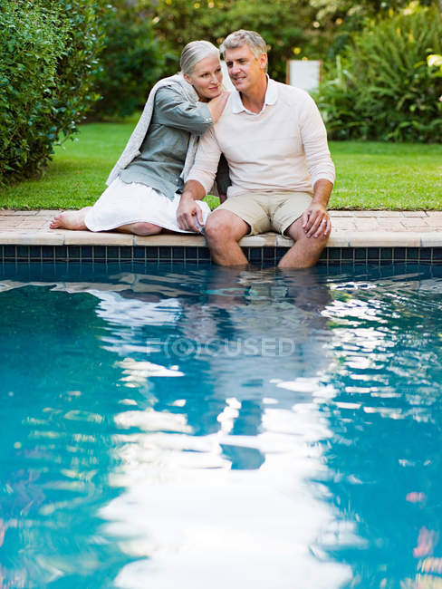 Couple assis au bord de la piscine dans le jardin — Photo de stock