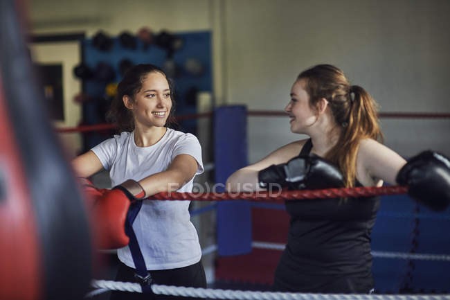 Jovens boxers do sexo feminino encostados contra cordas do anel de boxe conversando — Fotografia de Stock