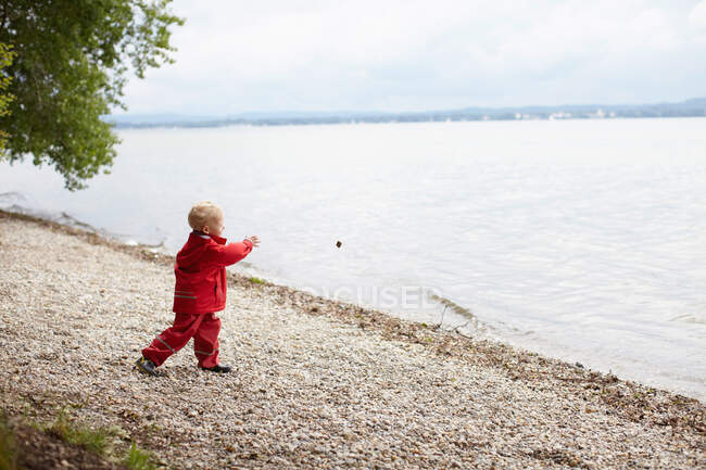 Chico lanzando rocas al lago - foto de stock