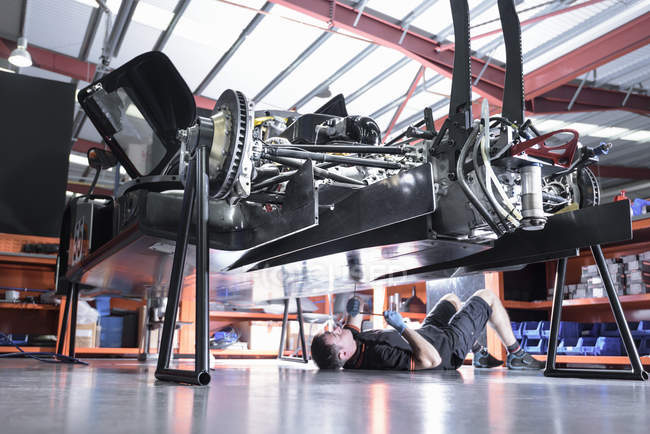 Engineer working underneath car in racing car factory — Stock Photo