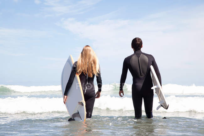 Jovem casal caminhando para o mar segurando pranchas de surf, visão traseira — Fotografia de Stock