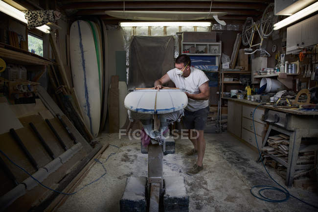 Homem maduro lixando uma prancha de surf em sua oficina — Fotografia de Stock