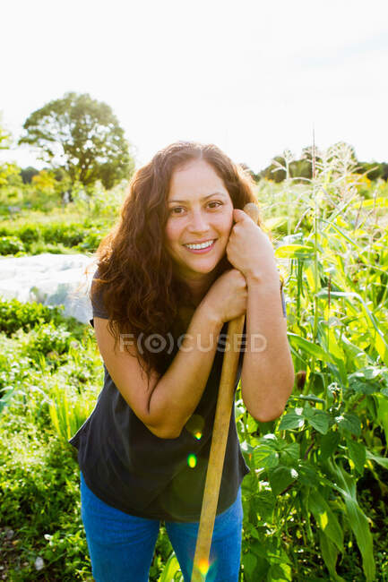 Porträt einer jungen Frau, die sich in Schrebergarten an Gartengerät lehnt — Stockfoto