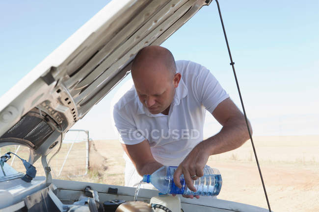 Чоловік наливає воду на двигун автомобіля — стокове фото