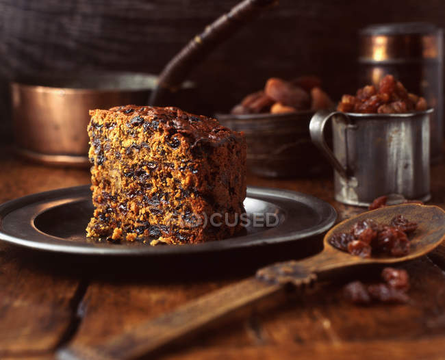 Slice of fruitcake on pewter plate with wooden spoon — Stock Photo