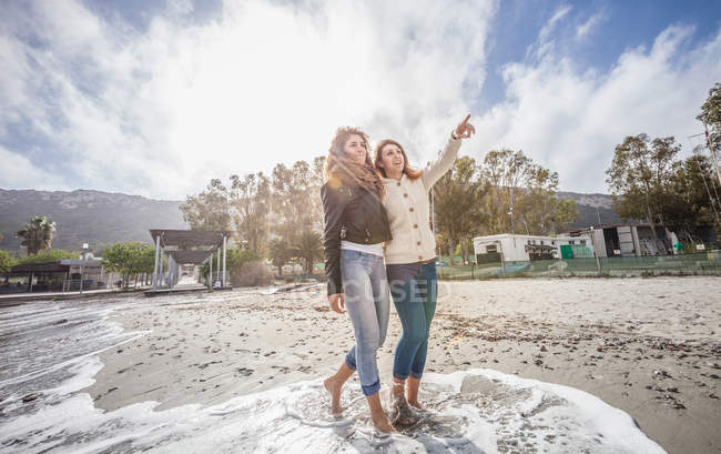 Zwei junge Freundinnen spazieren barfuß am Strand in Italien — Stockfoto