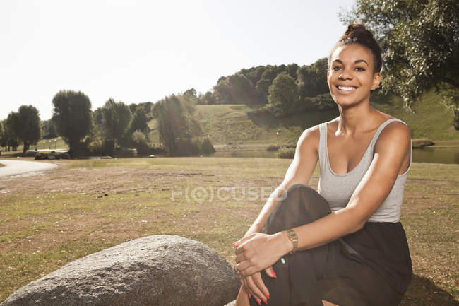 Junge Frau sitzt im Park und blickt in die Kamera — Stockfoto